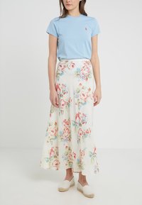 T-shirt di cotone azzurro chiaro abbinato a una lunga gonna bianca fluida con grandi motivi floreali rossi e blu. Indossato con espadrillas beige.