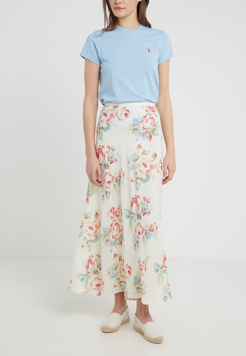 T-shirt di cotone azzurro chiaro abbinato a una lunga gonna bianca fluida con grandi motivi floreali rossi e blu. Indossato con espadrillas beige.