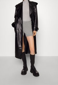 Manteau trench en cuir noir, haut en tricot gris, shorts gris, bottes noires jusqu'aux genoux avec bout carré et semelle épaisse, design élégant et moderne.