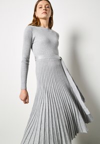 Grijze lange mouwen geribbelde jurk met een nauwsluitende bovenkant en geplooide rok, met een bijpassende riem in de taille en een gestructureerde afwerking.