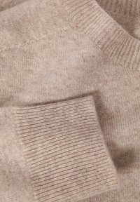 Jasnoróżowy sweter z dzianiny o gładkiej fakturze, z prążkowanymi mankietami i subtelnym wzorem w różnych odcieniach na całej tkaninie.