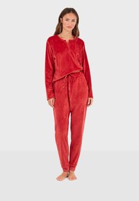 Ensemble de pyjama en velours rouge comprenant des manches longues, un col entièrement boutonné et un pantalon à cordon de serrage avec un détail décoratif subtil. Texture douce.