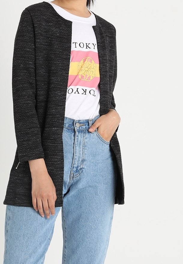 Personne portant un cardigan gris foncé ouvert devant, un t-shirt blanc avec un motif rose et jaune, et un jean taille haute bleu clair.