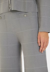 Traje de tela gris texturizada con un patrón de cuadrícula. La chaqueta presenta un detalle de botón, mientras que los pantalones tienen un corte de pierna ancha y un acabado texturizado.