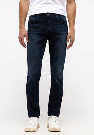 Vaqueros de denim azul oscuro con un diseño de pierna recta, que cuentan con cinco bolsillos y un ligero desgaste. Llevados con zapatillas blancas.