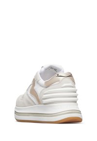 Zapatilla ligera en blanco con acentos beige y textura de ante. Presenta una suela gruesa con surcos y una franja plateada en la entresuela.