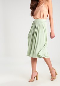 Gonna midi plissettata verde chiaro con vita elasticizzata, abbinata a un top pesco con spalline sottili e sandali con tacco blocco color nocciola.