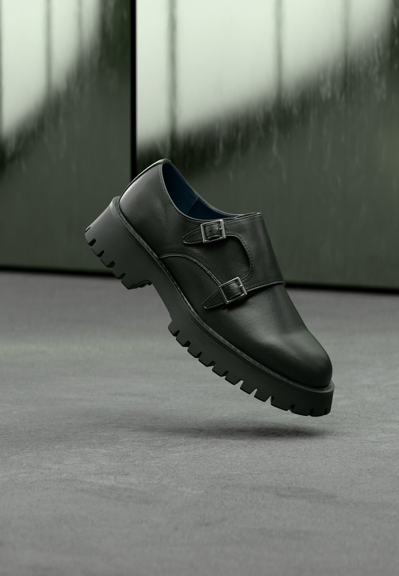 Chaussure en cuir noir avec double boucle, pointe arrondie et semelle épaisse en caoutchouc texturé. Design minimaliste avec intérieur bleu contrastant.