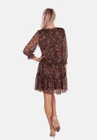 Braunes Tierdruckkleid mit langen durchsichtigen Ärmeln, gerafftem Taillenbereich und gestuftem, rüschiertem Saum. Kombiniert mit beigen High Heels.