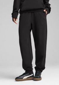 Sorte sweatpants lavet af blødt stof, der har en afslappet pasform med sidelommer og et broderet logo. Matchet med sorte og hvide sneakers.