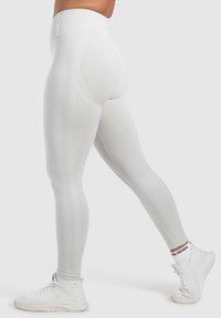 Weiße, hochtaillierte Leggings mit gerippter Textur und figurbetontem Design, versehen mit konturierenden Akzenten und kombiniert mit leichten weißen Sneakers.