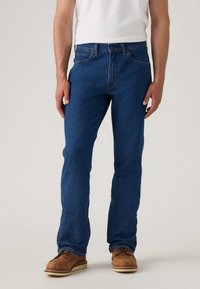 Vaqueros de denim azul con corte recto, diseño de cinco bolsillos y un cierre clásico de botón. Combinados con zapatos marrones decordones.