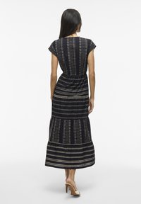 Abito lungo di un blu navy scuro con maniche a cappuccio, vita stretta e tessuto decorato con strisce orizzontali e dettagli geometrici.