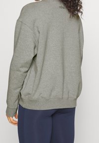 Šedá mikina s volným střihem, žebrovanými manžetami a lemem. Na zadním výstřihu má jemné logo. V kombinaci s námořnickými legínami.