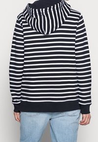Sudadera de rayas azul marino y blanca con capucha ajustable, puños y dobladillo acanalados. Hecha de una tela suave, presenta un corte relajado.