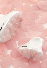 Deux outils de massage SkinIron sur des surfaces en pierre rose. Les outils sont blancs avec des extrémités arrondies et bulbées ; le plus grand a 12 nodules texturés, le plus petit en a 8.
