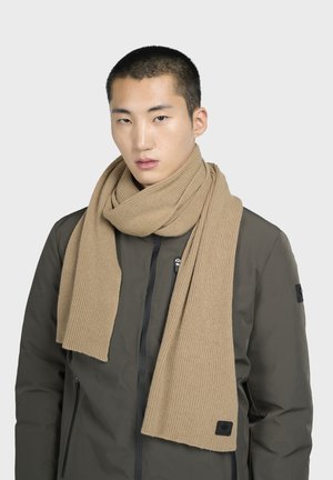 Bufanda de canalé beige hecha de material suave, puesta alrededor del cuello. Combinada con una chaqueta verde oscuro con acentos de hardware negro.