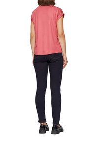 Roze T-shirt met korte mouwen en opgerolde mouwen, gecombineerd met donkerblauwe skinny jeans. Minimale stiksels en een casual pasvorm.