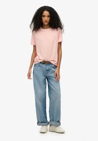 Różowa bawełniana koszulka, luźny krój, krótki rękaw, związana w talii. Połączona z jasnoniebieskimi dżinsami, podwiniętymi na kostkach. Białe sneakersy.