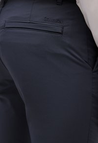 Pantaloni blu navy realizzati in tessuto liscio, dotati di tasca sul retro e logo "Calvin Klein" in rilievo sulla cintura. Vestibilità moderna con un design elegante.