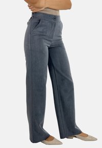 Pantalons réglés gris avec une texture lisse, jambes larges, deux poches latérales et une fermeture à bouton. Accordés avec des chaussures beige à enfiler.