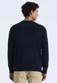 Dunkelblauer Strickpullover mit strukturiertem Muster, ausgestattet mit einem Rundhalsausschnitt und Rippbündchen, von hinten vor einem hellen Hintergrund gezeigt.