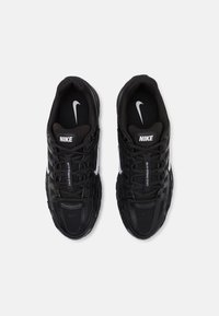 Baskets Nike noires avec une tige en mesh, des superpositions texturées, des accents de logo blancs et des lacets plats. Conçues pour le confort et la respirabilité.