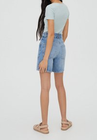 Pantalones cortos de mezclilla de cintura alta, lavado azul claro, diseño de cinco bolsillos, dobladillo deshilachado, combinados con una camiseta ajustada azul claro y sandalias beige.