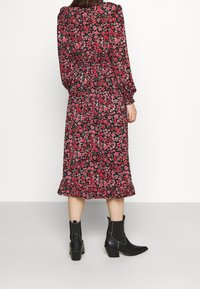 Robe midi florale avec un fond noir, présentant des fleurs rouges et roses, une taille élastique et des manches longues. Associée à des bottines noires.