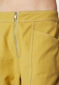 Gula bomullsbukser med en silverdragkedja, kontrasterande vit sömnad och en hög midja med sidfickor.