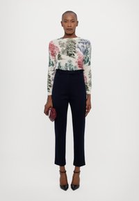 Pletený sveter s farebnými vzormi stromov v červenej, zelenej a modrej farbe, skombinovaný s přizpůsobenými námorníckymi nohavicami a čiernymi špicatými podpätkami.