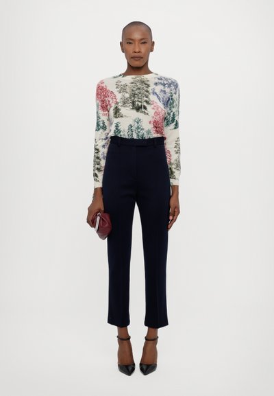 Knitted sweater featuring colorful tree patterns in red, green, and blue, paired with tailored navy trousers and black pointed heels.
