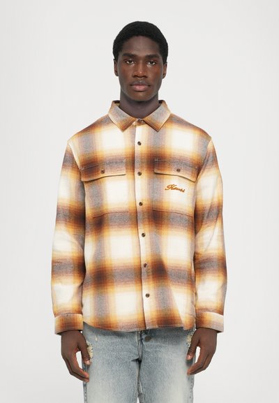 Camisa de cuadros en tonos marrón, crema y gris. Presenta un diseño de botones en la parte delantera, dos bolsillos en el pecho y un logo bordado en el lado izquierdo. Mezcla de algodón.