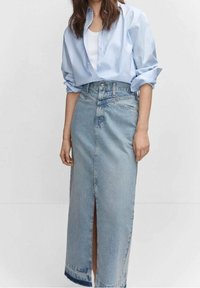 Vaaleansininen farkkuhame, jossa on etuaukko, raaka helma ja korkea vyötärö. Mallilla on päällään väljä vaaleansininen napitettava paita.