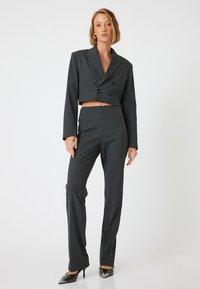 Donkergrijze op maat gemaakte cropped blazer met dubbele knopen, gecombineerd met bijpassende hoge taille rechtlopende broeken en puntig schoenen.