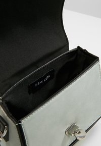 Grønne faux læder håndtaske med en sort indvendig. Har en sølvlås og et mærke med teksten "NEW LOOK." Struktureret design med rene linjer.