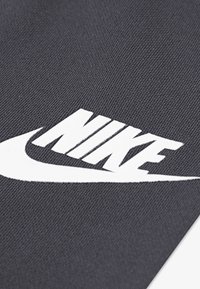Nike-Logo in Weiß auf einem strukturierten dunkelgrauen Stoffhintergrund, mit einem Swoosh-Design mit kräftigen Linien und markanter Schrift.
