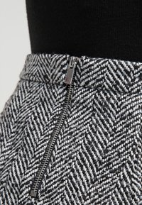 Jupe en tissu à chevrons tissés en noir et blanc avec un détail de fermeture éclair métallique. Gros plan sur la ceinture et les caractéristiques de la texture.