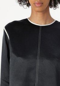Black top made from a smooth fabric, featuring a round neckline with a contrasting trim and central stitching down the front.