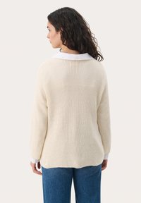 Cream-colored sweater with a textured knit design. Features a white collar and relaxed fit, paired with blue denim jeans.