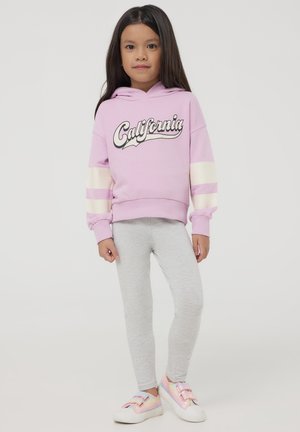 Fioletowa bluza z kapturem z napisem "California", kremowe paseczki na rękawach, zestawiona z szarymi legginsami i pastelowymi sneakersami z podwójnymi paskami.