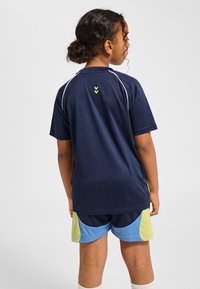 Sportströja i marinblått med korta ärmar, vita sömmar och grönt inslag bak. Matchas med flersfärgade shorts i blått och grönt.