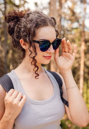 Black sunglasses with blue mirrored lenses, featuring a geometric shape and a textured frame. The person wore a gray tank top and a backpack.