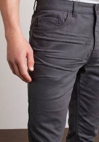 Jeans grigi slim-fit realizzati in un resistente tessuto misto cotone, con cinque tasche. Il tessuto ha una consistenza liscia con leggere pieghe.