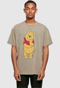 Brun oversized t-skjorte med et grafisk trykk av Ole Brumm i rød skjorte. Har kort erm, rund halsutskjæring og en falmet tekstur.