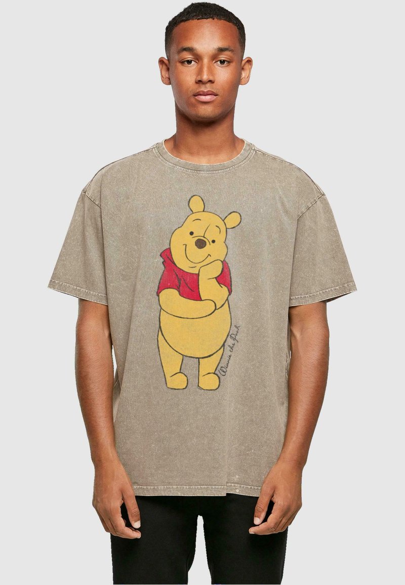 Brun oversized t-skjorte med et grafisk trykk av Ole Brumm i rød skjorte. Har kort erm, rund halsutskjæring og en falmet tekstur.