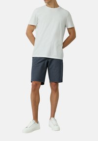 Weißes Baumwoll-T-Shirt kombiniert mit dunkelblauen karierten Shorts. Weiße Sneakers runden den Look ab und zeigen ein lässiges, atmungsaktives Design.