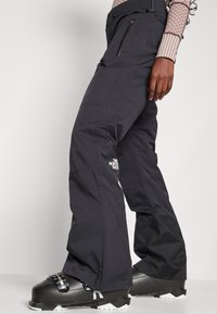 Svarte vanntette skibukser med rett snitt, med glidelåslommer og North Face-logo, laget av slitesterkt stoff.
