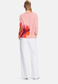 Pink sweater with a textured finish, three-quarter sleeves, featuring a colorful floral pattern on the back. Paired with white wide-leg pants.