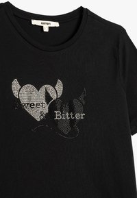 Sort kortærmet t-shirt med rhinestone-detaljer i hjerteformer med teksten "Sweet" og "Bitter", struktureret stof.
